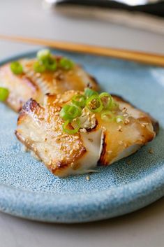 two pieces of fish on a blue plate with chopsticks