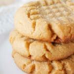 three peanut butter cookies stacked on top of each other with a cup of coffee in the background