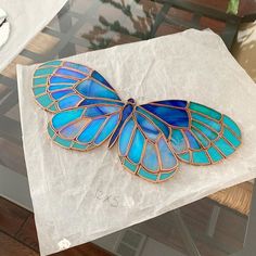 a blue butterfly brooch sitting on top of a white piece of paper next to a glass table