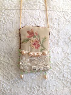 an embroidered purse with pearls and flowers hanging on a lace tablecloth covered wall ornament