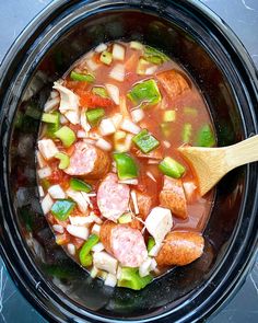 a crock pot filled with soup and vegetables next to a wooden spoon in it