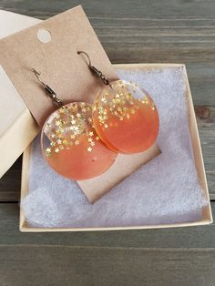 Beautiful and fiery sunset orange resin disk earrings, filled with gold stars. Vibrantly orange circle half circles, paired its clear stary other half, perfectly preserved in resin for it's natural beauty. Vividly colorful, lightweight, and dazzling stars in every light setting ♥ Be sure to check out the ORANGE EARRINGS section at EarringsbyLCreations for all beautiful orange colored earrings available! https://www.etsy.com/shop/EarringsByLCreations?section_id=28420987 Made with quality material Orange Dangle Resin Earrings, Orange Resin Dangle Earrings, Orange Resin Earrings, Fiery Sunset, Orange Star, Disk Earrings, Orange Resin, Orange Circle, Gold Star Earrings