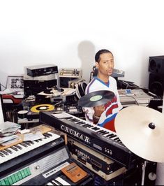 a man is holding a record player in front of an assortment of musical instruments and keyboards