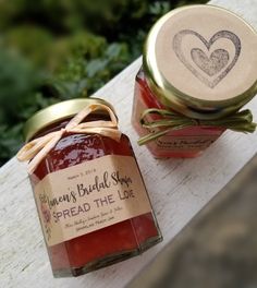 two jars of jam sitting next to each other on a wooden table with a heart sticker