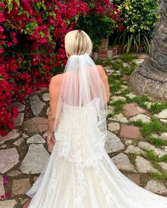 the back of a bride's wedding dress as she stands in front of flowers