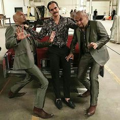 three men standing next to each other in front of a car