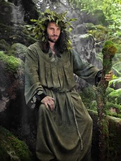 a man with long hair wearing a green robe and holding a stick in his hand