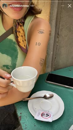 a woman sitting at a table with a cup and saucer in her hand, holding a spoon