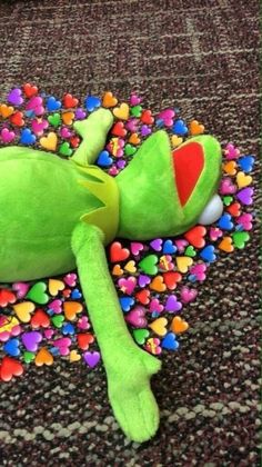 a green stuffed animal laying on top of a carpet covered in candy heart candies