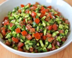 cucumber and tomato salad in a white bowl on top of a wooden table