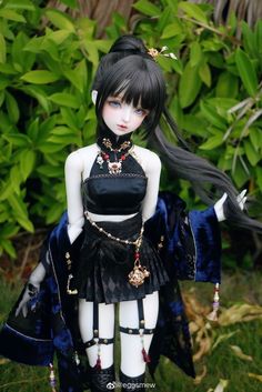 a doll with long black hair wearing a dress and necklace, standing in front of some bushes