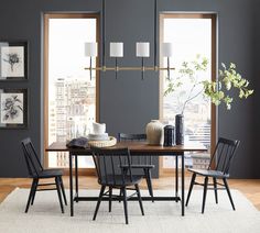 a dining room table with four chairs and a rug in front of two windows overlooking the city