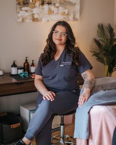 a woman sitting on top of a stool next to a bed with a tattoo on her arm