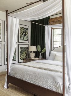 a canopy bed in a bedroom with white drapes and paintings on the wall behind it