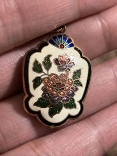 a hand holding a white and blue flower shaped broochel with green leaves on it