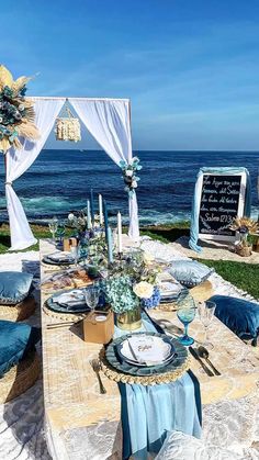 an outdoor table set up with blue and white linens for a wedding reception by the ocean