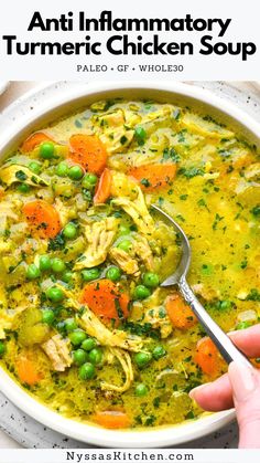 a hand holding a spoon over a bowl of chicken soup with peas and carrots