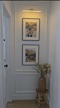 two framed pictures hang on the wall above a wooden stool in a hallway with wood flooring