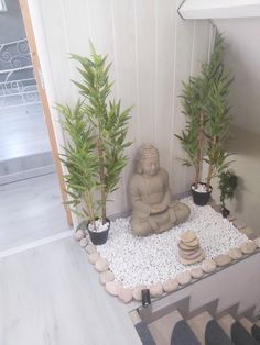 a buddha statue sitting on top of a table next to two plants and rocks in front of it