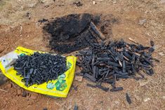 a pile of black sticks sitting on top of a dirt field next to a yellow bag