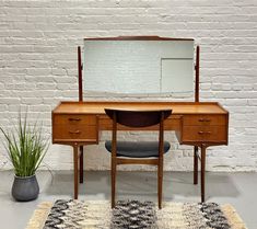 a desk with a mirror, chair and rug in front of a white brick wall