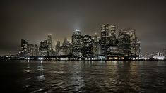 the city skyline is lit up at night with lights reflecting on the water in front of it