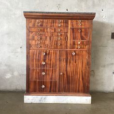 a wooden cabinet with many drawers and knobs on the front, against a concrete wall