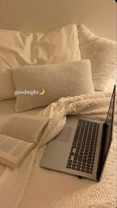 a laptop computer sitting on top of a bed next to an open book and pillow