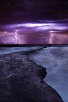 the sky is filled with purple and black clouds, while lightning strikes over the ocean