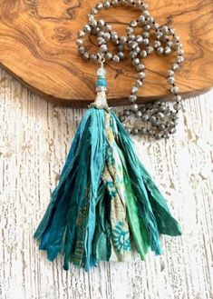 a necklace with tassels and beads hanging from it on a wooden board next to a beaded necklace