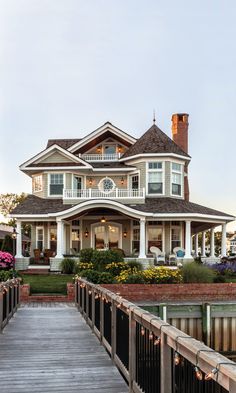 a large white house sitting on top of a lush green field next to a wooden bridge