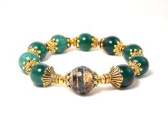 This gemstone piece has a vintage style feel a makes a stunning statement! Aventurine and Agate stones along with gold tones give this bracelet an elegant chic look! Faceted center bead creates a unique focal point while antique gold plated accents complement these beautiful semiprecious stones! Bracelet is made with strong elastic string allowing it to stretch to wrist size. Product Details .Semiprecious Agate & Aventurine stones. .Antique gold plated bead caps. .Gold plated brass metal spacers. .Clear elastic string. .Size of stones: 12 & 14mm. Bracelet Size: Small -  Wrist size - 6 inches. Outer dimension - 8½ inches. Medium -  Wrist size - 6½ inches. Outer dimension - 9 inches.  Large -  Wrist size - 7 inches. Outer dimension - 9½ inches.  Please be sure to check your wrist measurement Elegant Aventurine Beaded Bracelets For Healing, Gold Bracelets With Aventurine Natural Stones, Gold Bracelets With Natural Aventurine Stones, Handmade Elegant Aventurine Bracelets, Elegant Gold Agate Bracelets, Elegant Gold Agate Bracelet, Gold Aventurine Round Bead Bracelets, Gold Aventurine Beaded Bracelets With Natural Stones, Gold Beaded Aventurine Bracelets With Natural Stones