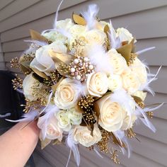 a bridal bouquet with white roses and feathers is held by someone's hand