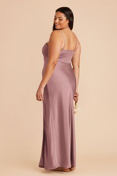 a woman in a long dress smiling and looking at the back of her dress, she is