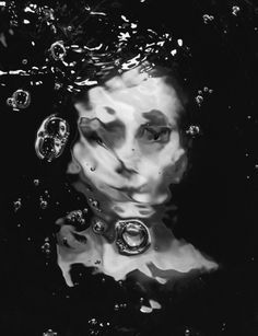 a black and white photo of a woman in the water with bubbles on her face