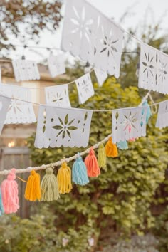 some tassels are hanging from a string in front of a house and trees