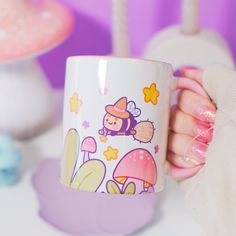 a person holding a coffee mug with cartoon characters on it and mushrooms in the background