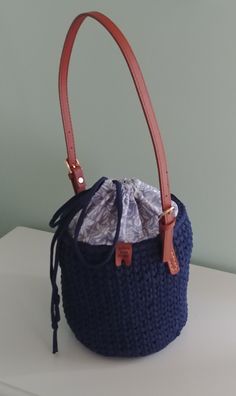 Navy Bucket Bag. Crocheted navy blue bucket bag, cotton blue and white fabric lining, inside pockets, drawstring closure, and brown leather buckle strap.  Dimensions: 23 inches round, 7.25 inches deep, 12 inch strap drop.  Surface washable.  Thank you for visiting YellowRoseRetail.com! Daily Use Bucket Hobo Bag With Leather Trim, Travel Bucket Bag With Leather Trim, Casual Blue Bucket Bag With Adjustable Strap, Blue Bucket Bag For Shopping, Casual Blue Crossbody Bucket Bag, Crochet Bucket Bag With Removable Pouch, Blue Bucket Bag With Braided Handles, Blue Bucket Bag With Braided Handles For Shopping, Casual Crochet Bucket Bag With Leather Handles