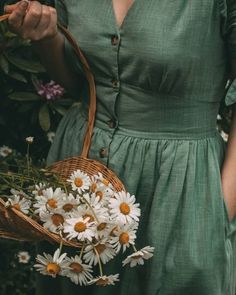 a woman in a green dress holding a basket with daisies on the outside and flowers inside