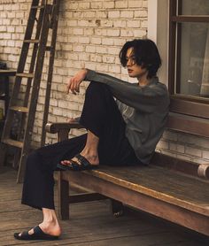 a woman sitting on top of a wooden bench next to a brick wall and ladder