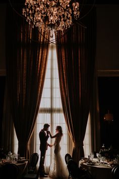 a bride and groom kissing in front of a chandelier at their wedding reception