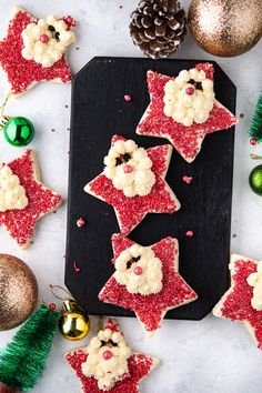 christmas cookies decorated to look like santas and reindeers on a cutting board with ornaments around them