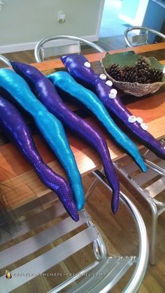 three purple and blue plastic worms sitting on top of a table next to a bowl