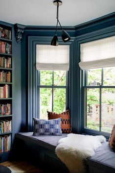 a window seat in front of two windows with bookshelves and pillows on it