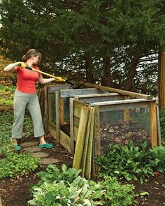 a woman standing next to a pile of wooden crates filled with plants and vegetables in a garden