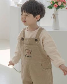 a little boy that is standing up with his hands in the air and wearing overalls