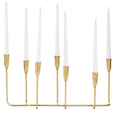 six white candles are lined up in a row on a brass stand with gold tips