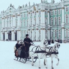 two horses pulling a carriage in front of a large green and white building with gold trim