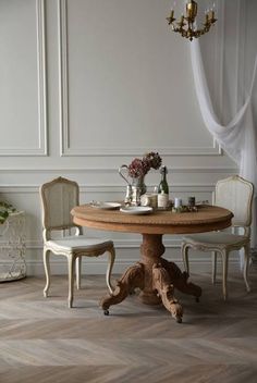 a dining table with two chairs and a vase on top of it in front of a white wall