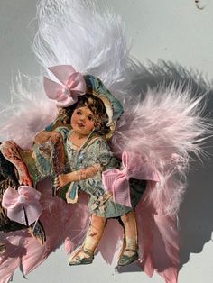 a doll with pink feathers and a hat on it's head sitting on a chair